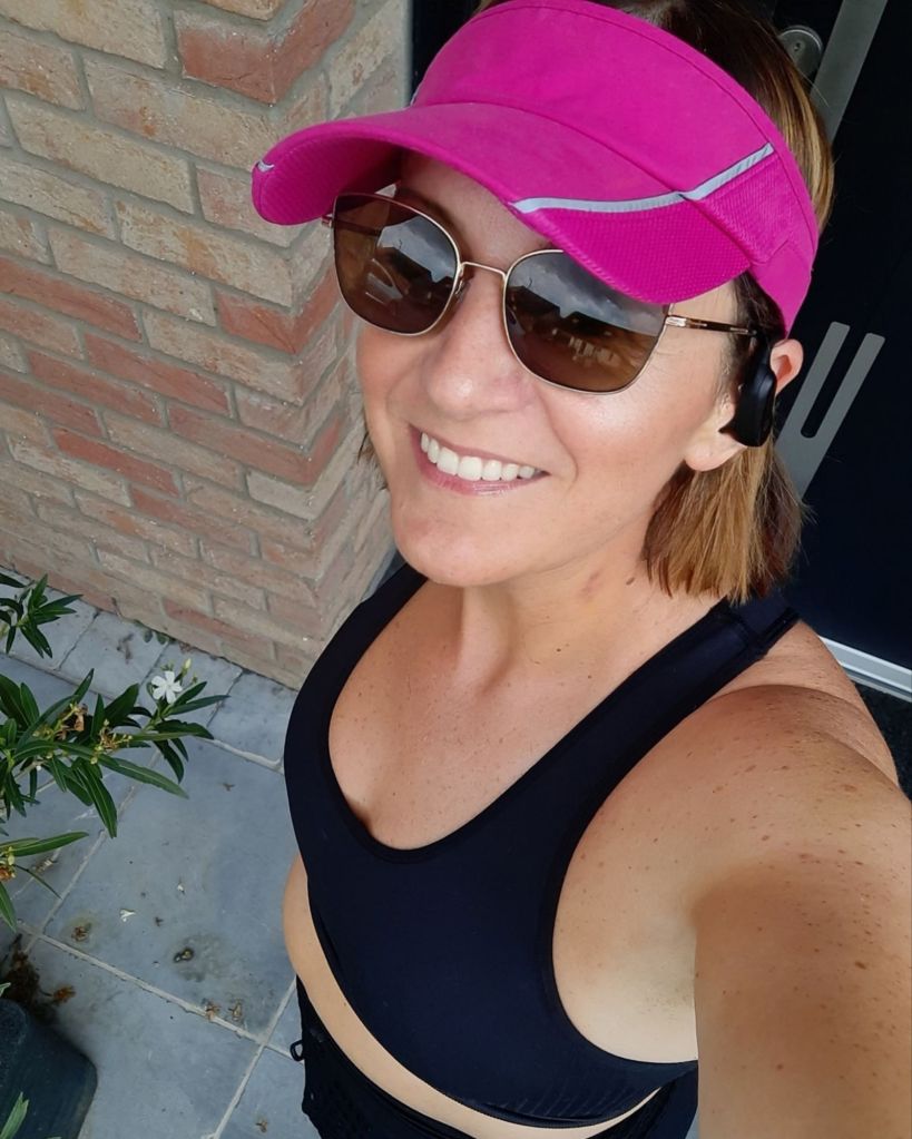 Femme souriante en tenue de jogging, visière rose et lunettes de soleil, incarnant l'énergie après 40 ans