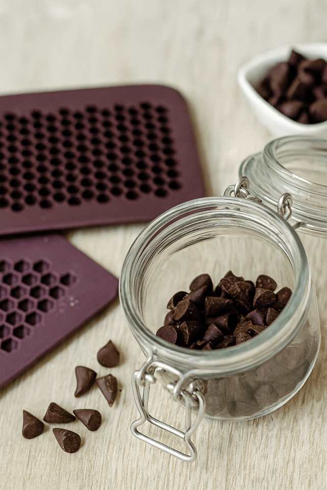 Pépites de chocolat noir maison dans un bocal en verre, moules en silicone bordeaux en arrière plan